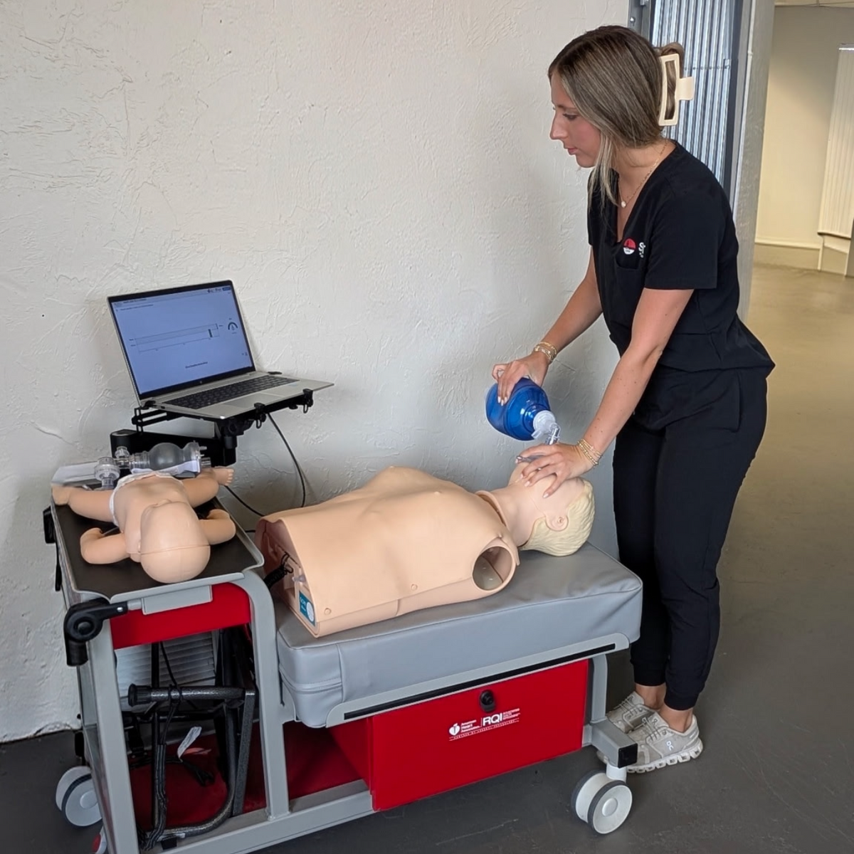 Person using a training device with mannequins and a laptop in a room.